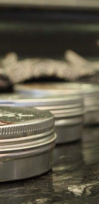 Een rij metalen blikjes haarwax op een donker marmeren blad