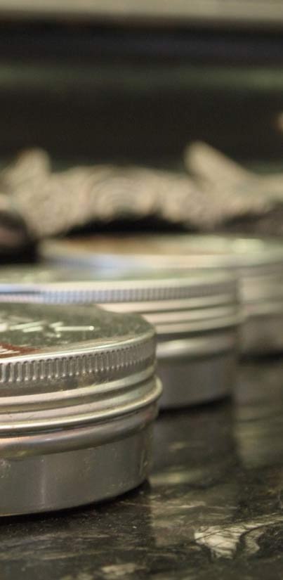 Een rij metalen blikjes haarwax op een donker marmeren blad