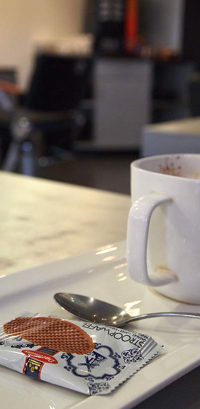 Een kop koffie met een stroopwafel en een lepeltje op een wit dienblad