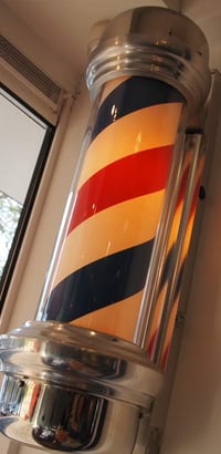 De verlichte barberpaal in rood, donkerblauw en crème bij het raam