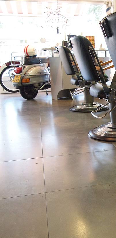 De salon met een crèmekleurige scooter naast de zwarte kappersstoelen, met daglicht door de ramen